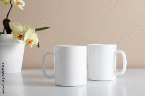 Fototapeta Naklejka Na Ścianę i Meble -  Two white coffee mug mockup with orchid flower. Empty cup mock up for design. Front view.