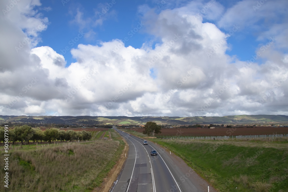 Landscape, asphalt road across the plain, leading to hills, against blue sky and white clouds background