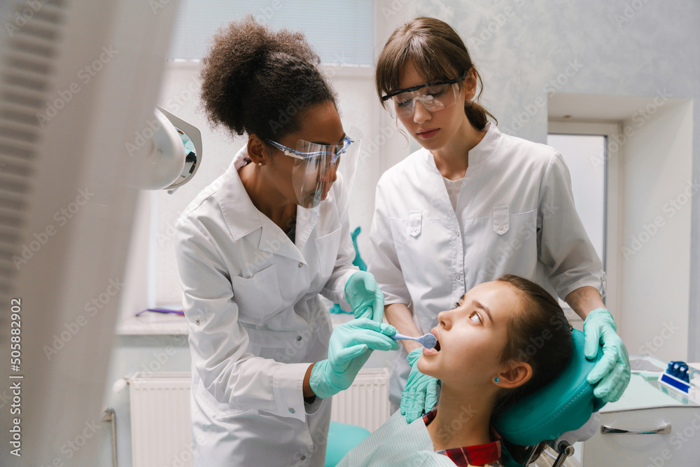 Two multiracial dentists wearing lab coats working in dental clinic Two multiracial dentists wearing lab coats working in dental clinic