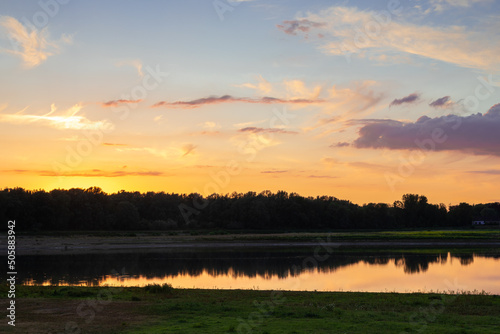 Beautiful sunset full of colors and dramatic clouds at the border between the Netherlands and Belgium where the countries are split by the river Meuse and wild horses graze freely in nature photo