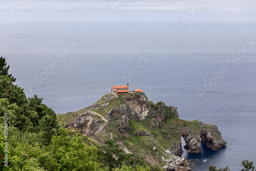 Cantabrian Sea ceaselessly erodes rocky coast creating tunnels, arches, and caves on Gaztelugatxe island with 9th-century church on 80 meters above sea level top. Biscay, Basque Country