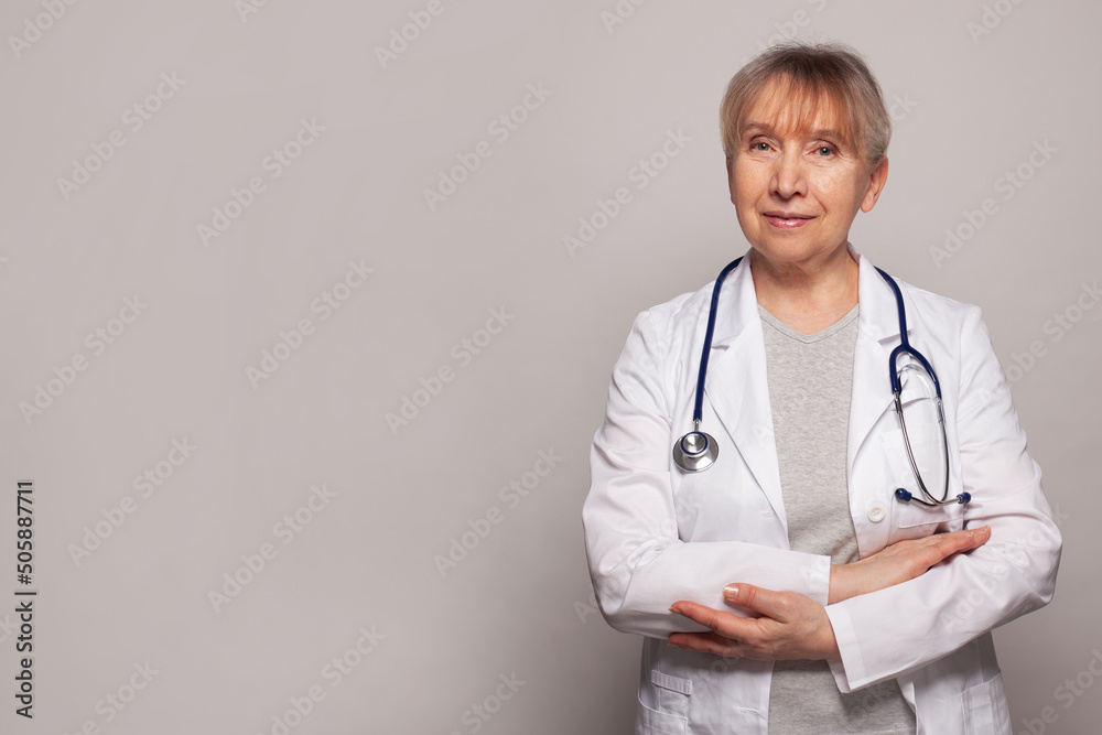 Smiling happy senior doctor pointing on grey background Smiling happy senior doctor pointing on grey background