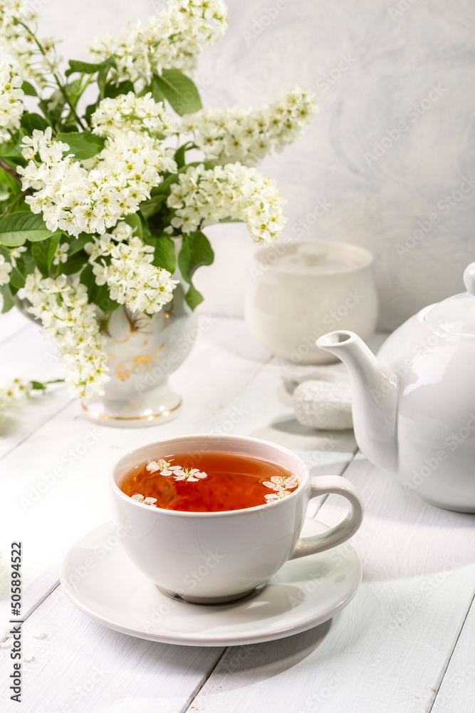 Useful spring tea with bird cherry in a white cup on a light background Useful spring tea with bird cherry in a white cup on a light background