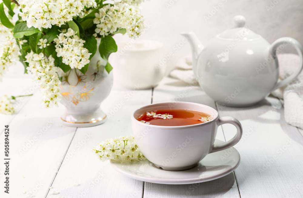 Useful spring tea with bird cherry in a white cup on a light background