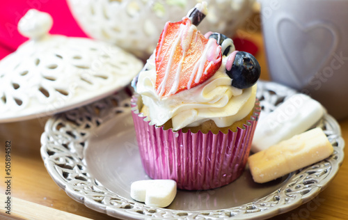 Obraz na płótnie Romantic cupcake decorated with cream, strawberry, and berry fruits on a Victorian openwork plate and wooden tray. Elegant dessert beautifully served among coffee mug and old vintage porcelain. w salonie
