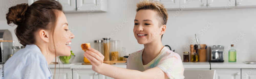 happy pangender person feeding partner with delicious croissant, banner. happy pangender person feeding partner with delicious croissant, banner.