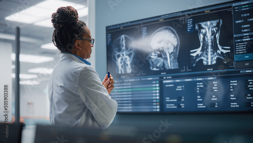 Medical Science Hospital: Confident Black Female Neurologist, Neuroscientist, Neurosurgeon, Looks at TV Screen with MRI Scan with Brain Images, Thinks about Sick Patient Treatment Method. Saving Lives