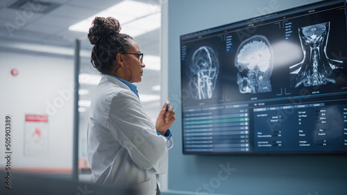 Medical Science Hospital: Confident Black Female Neurologist, Neuroscientist, Neurosurgeon, Looks at TV Screen with MRI Scan with Brain Images, Thinks about Sick Patient Treatment Method. Saving Lives photo