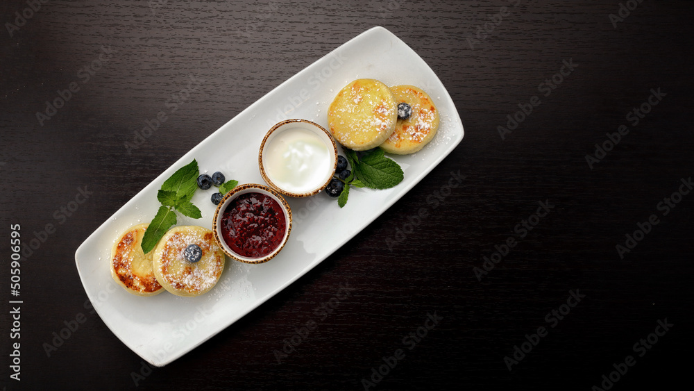 Breakfast, cheesecakes with two sauces. mint and blueberries, on a dark background Breakfast, cheesecakes with two sauces. mint and blueberries, on a dark background