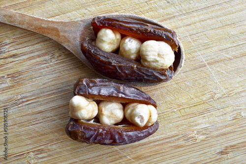 Dried hurma dates medjool grains, hazelnuts placed inside the date, on wooden spoon photo