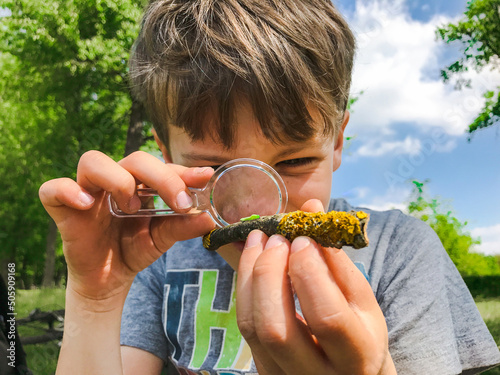 Boy with magnifying glass looking at a small green bug outdoors in a park. A little boy studying an insect with a magnifying glass in the nature. Boy holding a magnifying glass. Child examining a bug.