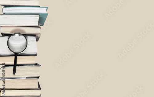 Banner with large books heap and magnifier. Research conducting, important data search, information analysis, preparing for exams concept. Copy space on pastel background. High quality photo photo