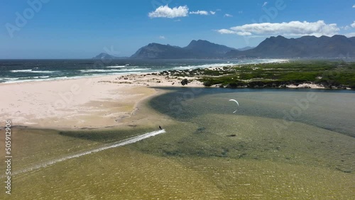 Kitesurfing near sandy coastline of South Africa with mountain range in horizon
