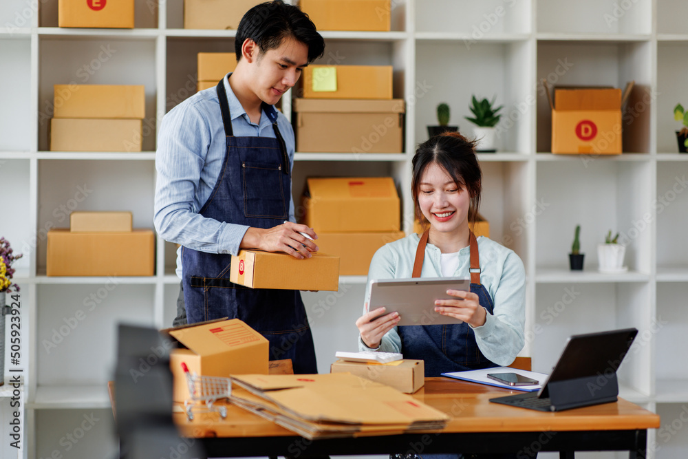 Startup small business SME. Two Young Asian business entrepreneurs using laptop computer check online orders and prepare to pack for customers. Successful SME business online concept. Startup small business SME. Two Young Asian business entrepreneurs using laptop computer check online orders and prepare to pack for customers. Successful SME business online concept.