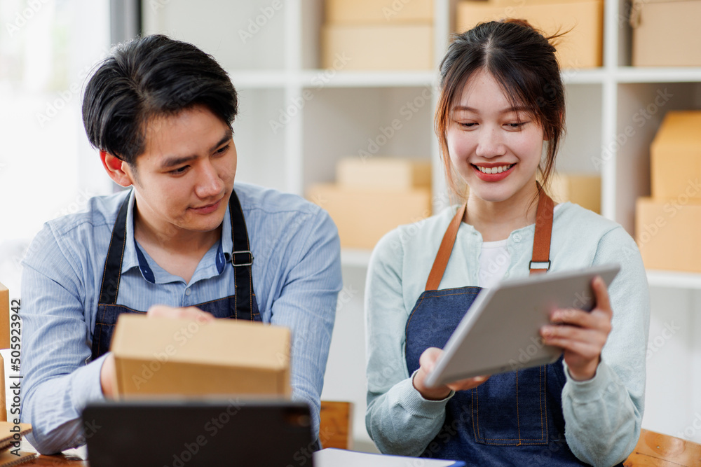 Startup small business SME. Two Young Asian business entrepreneurs using laptop computer check online orders and prepare to pack for customers. Successful SME business online concept. Startup small business SME. Two Young Asian business entrepreneurs using laptop computer check online orders and prepare to pack for customers. Successful SME business online concept.