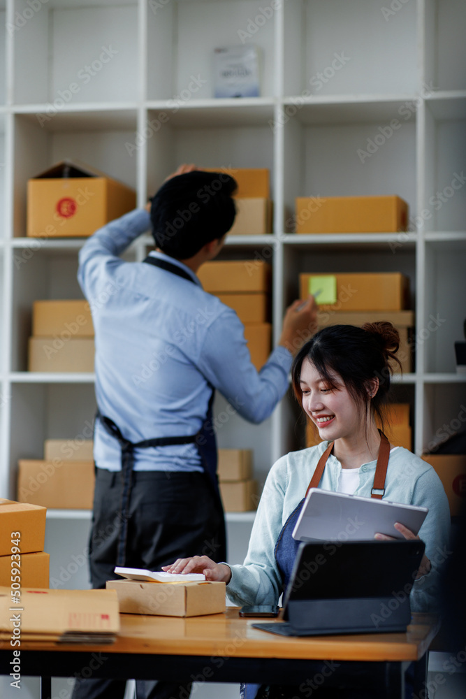 Startup small business SME. Two Young Asian business entrepreneurs using laptop computer check online orders and prepare to pack for customers. Successful SME business online concept. Startup small business SME. Two Young Asian business entrepreneurs using laptop computer check online orders and prepare to pack for customers. Successful SME business online concept.