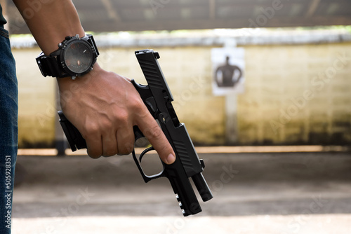 A gun shooter holds 9mm automatic pistol in right hand in front of the gun shooting range, concept for security, robbery, gangster and bodyguard training around the world. selective focus on pistol. photo