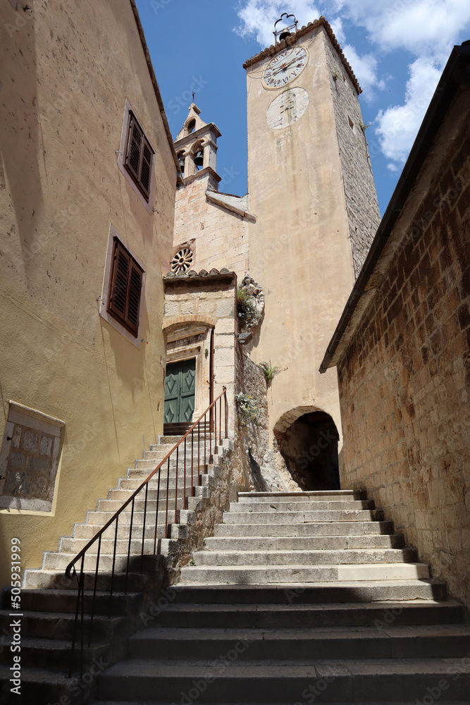 Narrow streets of the old town, stairs, stone houses, clock tower and bell tower against the blue sky, Omiš, Croatia