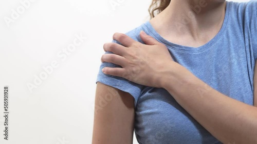 Woman massages sore shoulder with hand on white background, closeup. Woman rubs bruised shoulder with hand. Injury concept photo