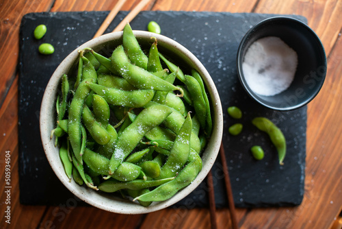 Steamed edamame sprinkled with sea salt on a dark stone board, top view