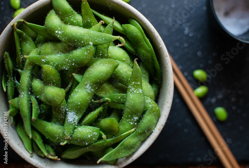Close-up of steamed edamame sprinkled with sea salt on a dark stone board, top view