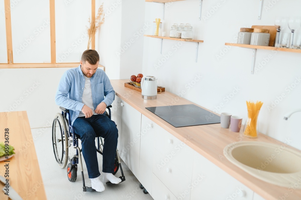 Young Disabled Man On Wheelchair In The Kitchen.
