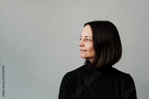 Woman with a black turtleneck sweater stands in front of a neutral gray background and look to the side