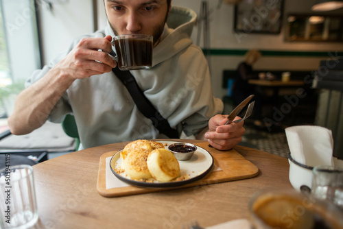 young man eats delicious cheesecakes in a cafe and drinks coffee © Victoriya Bulyha