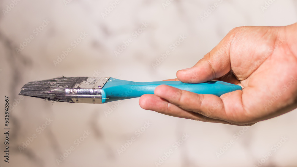 Close up male hand holding a medium size paint brush on abstract white background Close up male hand holding a medium size paint brush on abstract white background