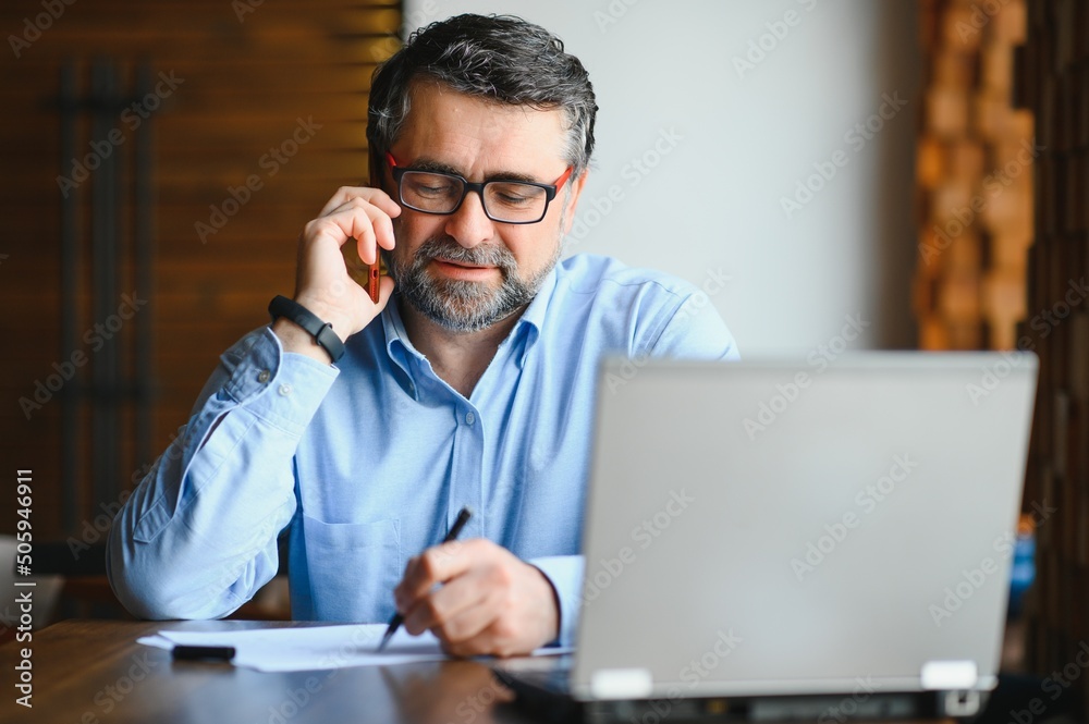 Male freelancer is working in a cafe on a new business project. Sits at a large window at the table. Looks at a laptop screen with a cup of coffee