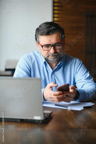 Male freelancer is working in a cafe on a new business project. Sits at a large window at the table. Looks at a laptop screen with a cup of coffee