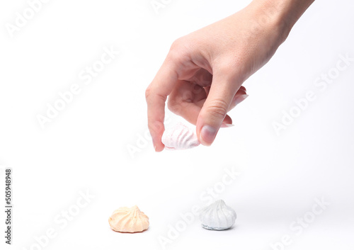 Woman hand chooses sweet colored meringue isolated on a white background.