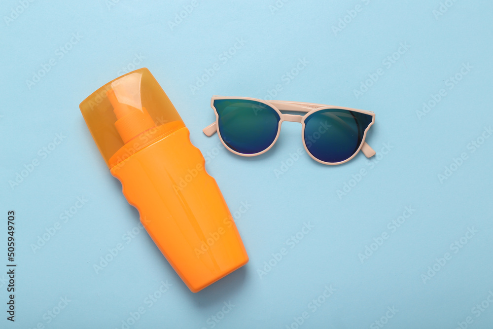 Resort, beach vacation, vacation concept. Sunglasses and a bottle of tanning cream on a blue background. Top view Resort, beach vacation, vacation concept. Sunglasses and a bottle of tanning cream on a blue background. Top view