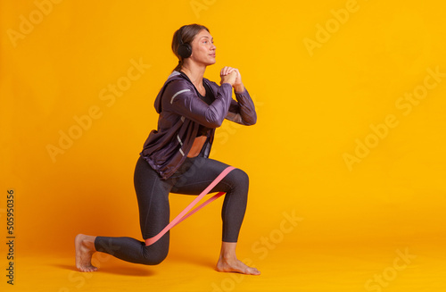 Workout concept. Athletic strong woman in sportswear practicing lunges .barefoot with fitness band on yellow background. Healthy lifestyle. Bodybuilding and fitness.