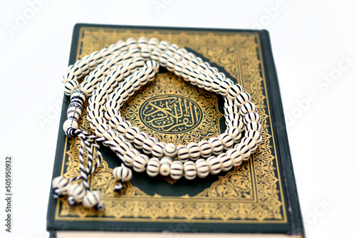 The holy Quran, Qur'an or Koran (the recitation) is the central religious text of Islam, believed by Muslims to be a revelation from God (Allah), isolated on white background with a rosary on it photo