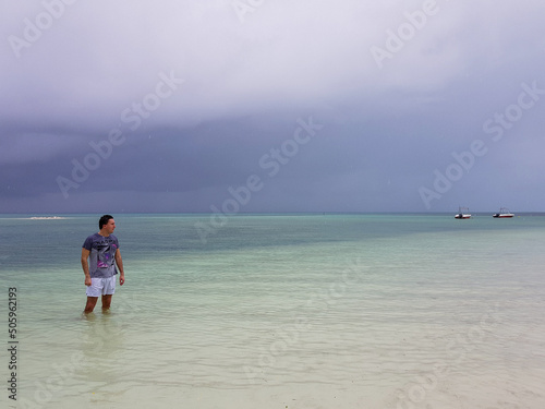 man in beachwear standing in water in ocean on tropical beach