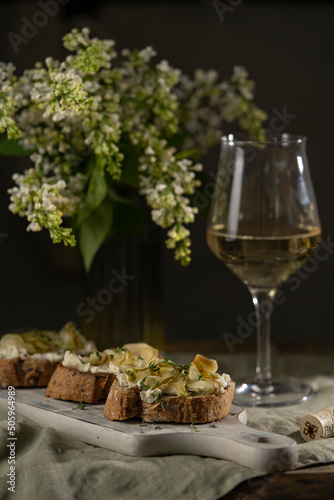 Bruschetta with gorgonzola cheese and pears, nuts on wooden table with textile, glass of white wine and beautiful flowers. Selective focus, copy space. 