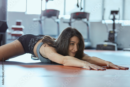 A flexible sportswoman is stretching in a gym.
