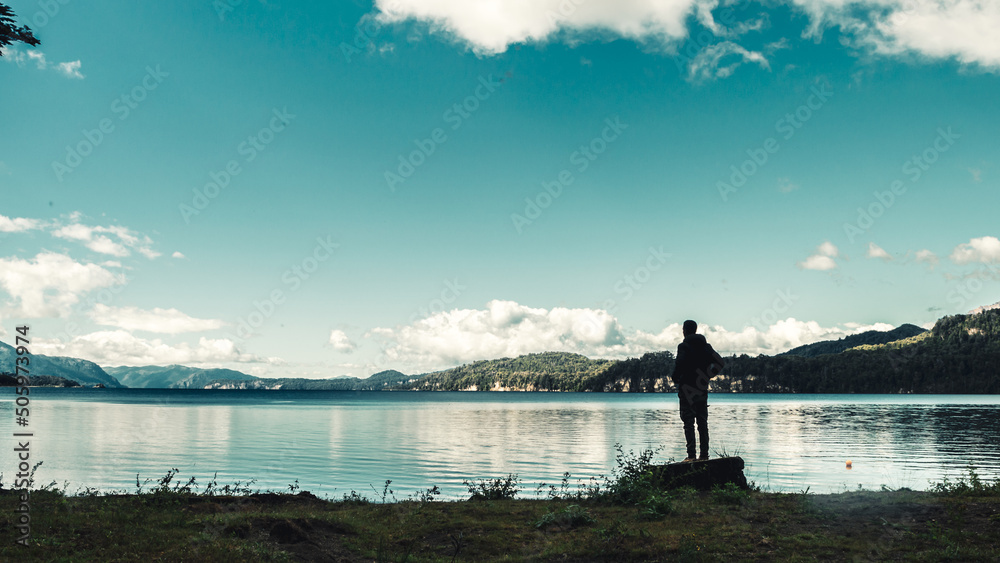 Young man standing on a felled tree overlooking a lake and mountain range in the background. Concept of life in nature. Andes Mountains, Argentina