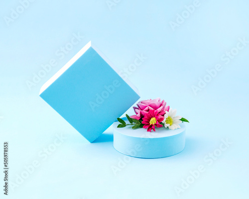 Creative minimal idea with pink flowers on a pastel blue cube and a circle on a blue background. Retro fashion aesthetic concept of the 80s or 90s. Cosmetics, makeup and fashion concept.