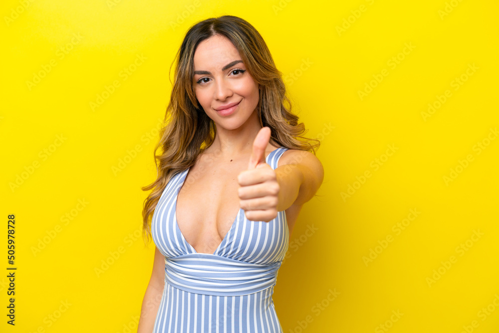 Young caucasian woman isolated on yellow background in swimsuit in summer holidays and with thumb up