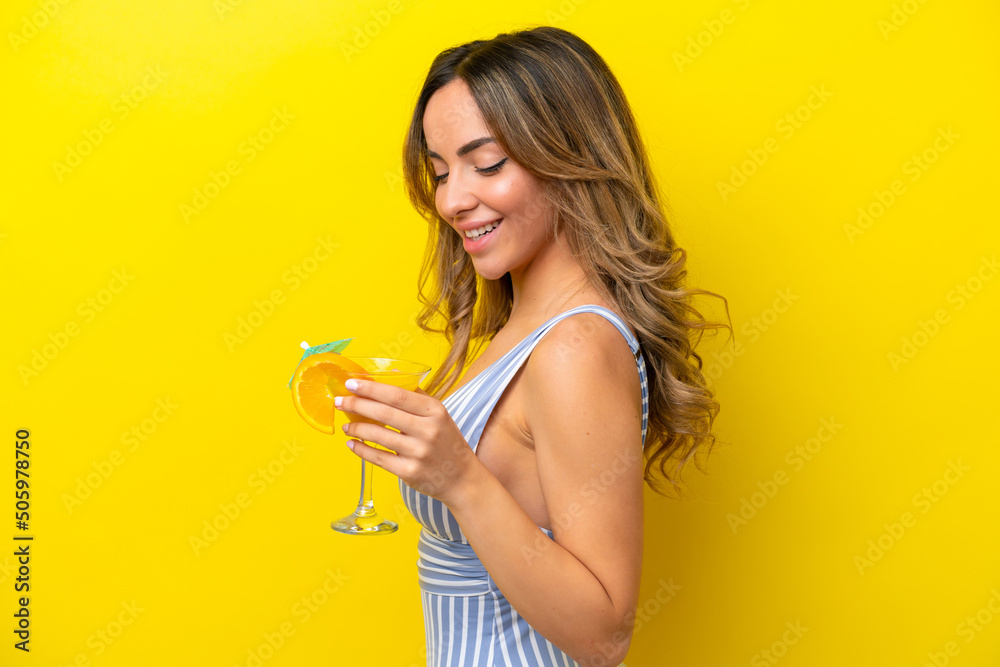 Young caucasian woman isolated on yellow background in swimsuit and holding a cocktail Young caucasian woman isolated on yellow background in swimsuit and holding a cocktail