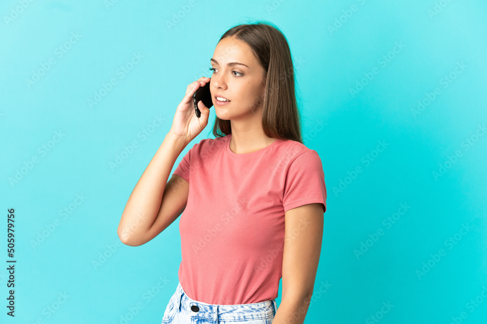 Young woman over isolated blue background keeping a conversation with the mobile phone Young woman over isolated blue background keeping a conversation with the mobile phone