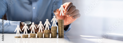 Human Hand Placing Human Figure On Increasing Stacked Coins