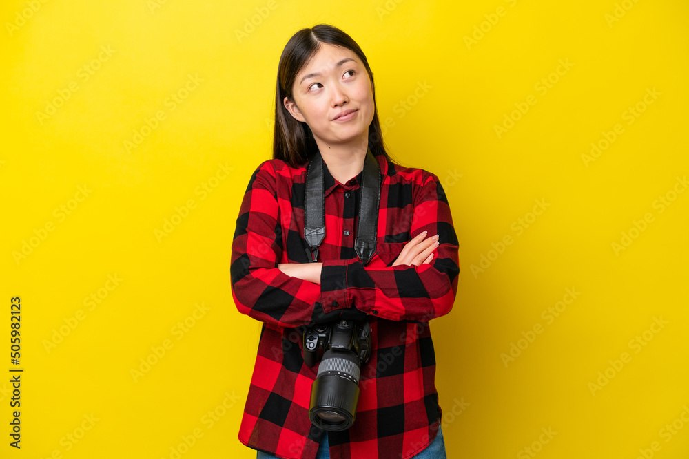Young photographer Chinese woman isolated on yellow background looking up while smiling Young photographer Chinese woman isolated on yellow background looking up while smiling