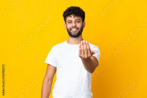 Young Moroccan man isolated on yellow background inviting to come with hand. Happy that you came