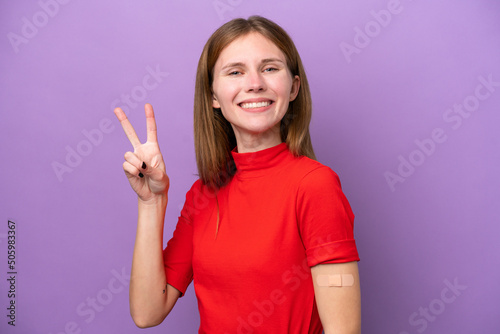 Young English woman wearing band-aids isolated on purple background smiling and showing victory sign