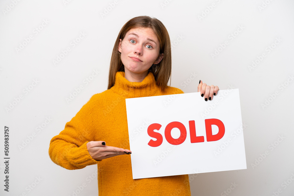 Young English woman isolated on white background holding a placard with text SOLD and pointing it Young English woman isolated on white background holding a placard with text SOLD and pointing it
