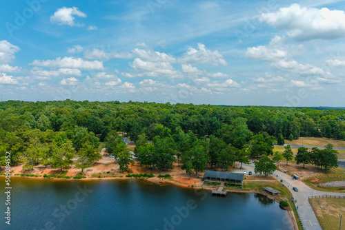 a gorgeous green rippling lake surrounded by lush green trees, grass and plants with blue sky and clouds and buildings among the trees at Lake Spivey Recreation Center in Jonesboro Georgia USA photo