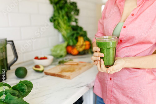 Green smoothie - healthy eating concept. faceless woman holding smoothie shake against kitchen home interior, focus on hands and glass